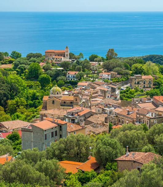 Vista panoramica di un borgo collinare con mare sullo sfondo.