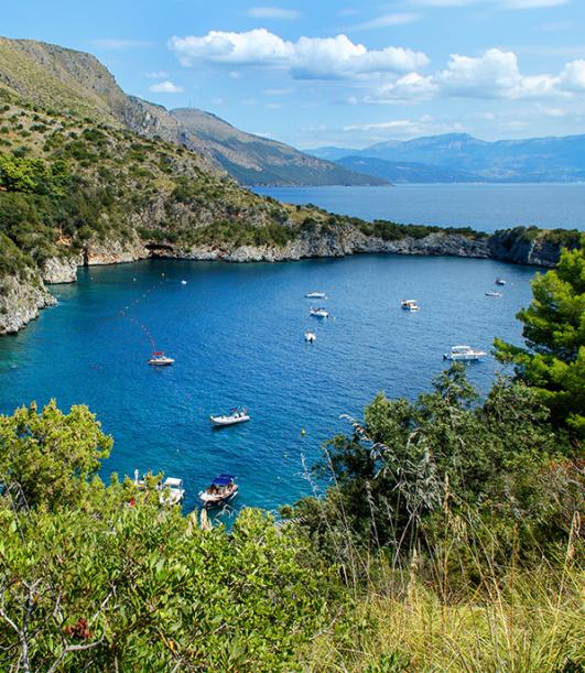 Baia con acque blu, circondata da colline e barche ancorate.