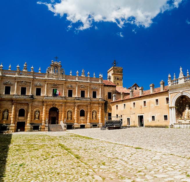 Storico monastero con architettura barocca, piazza lastricata e cielo sereno.