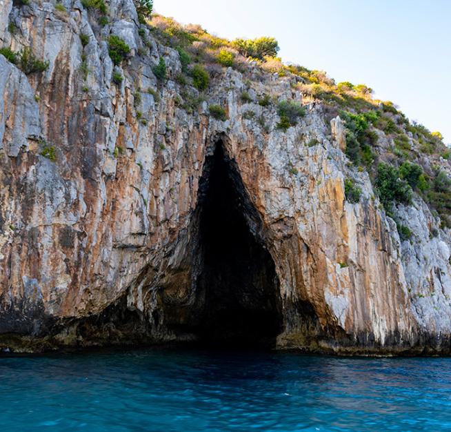 Grotta marina con acque turchesi e scogliere rocciose, circondata da vegetazione.